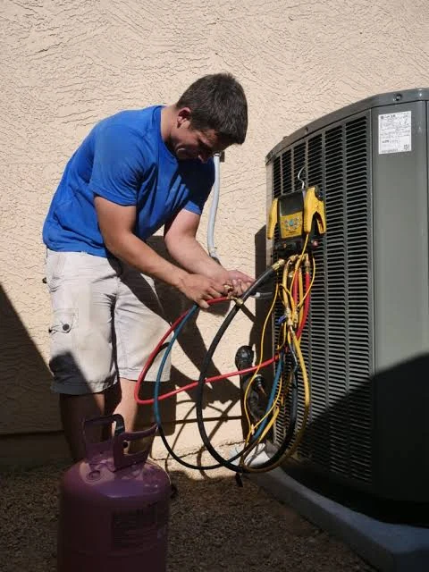 Technician connecting service gauges to an outdoor air conditioner