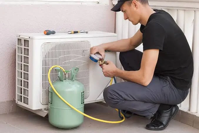 Technician checking a mini-split outdoor unit with refrigerant service equipment